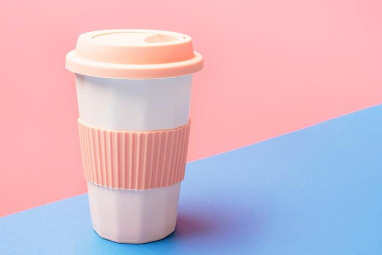 Reusable ceramic glass for coffee with silicone lid on a pink and blue background.