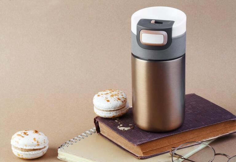 Golden stainless steel thermos for coffee and tea. Stylish mug for hot drinks with cap and valve