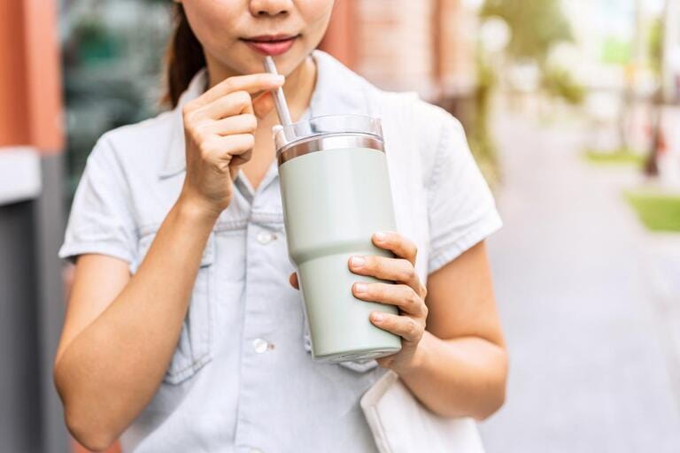 Young asian woman holding a reusable tumbler glass and walking in the city Young asian woman holding a reusable tumbler glass and walking in the city