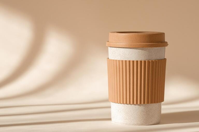 Reusable cup, biodegradable travel plastic coffee mug for take away. Sustainable bamboo eco friendly cup with silicone holder on natural shadow beige background. Reusable cup, biodegradable travel plastic coffee mug for take away. Sustainable bamboo eco friendly cup with silicone holder on natural shadow beige background.