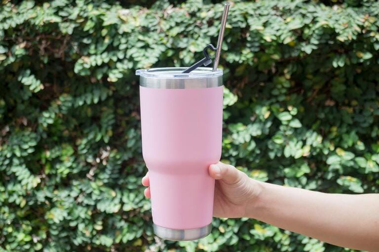 Hand on thermos tumbler mug with metal drinking straw Hand on thermos tumbler mug with metal drinking straw
