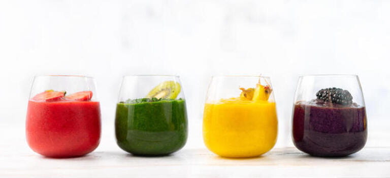 Four glasses with colorful detox smoothies on white background
