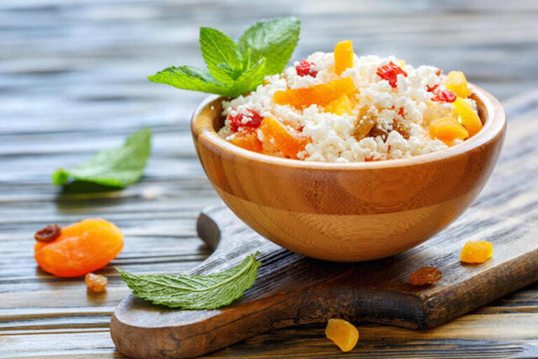 Cottage cheese with dried apricots and raisins in a wooden bowl.