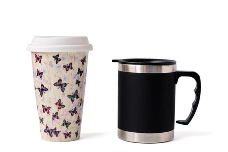 Two insulated coffee mugs on a wooden table. Two insulated coffee mugs on a wooden table.