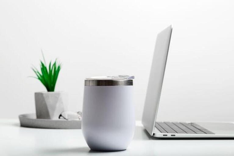 White thermo cup mock up on modern stylish workplace with laptop. Cup mockup. White thermo cup mock up on modern stylish workplace with laptop. Cup mockup.