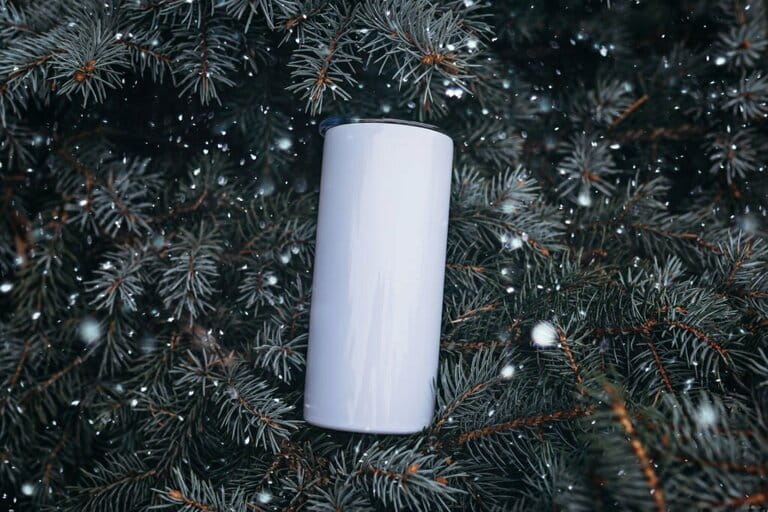 Empty white steel cup in hand on Christmas tree snow background. White steel tumbler mockup.