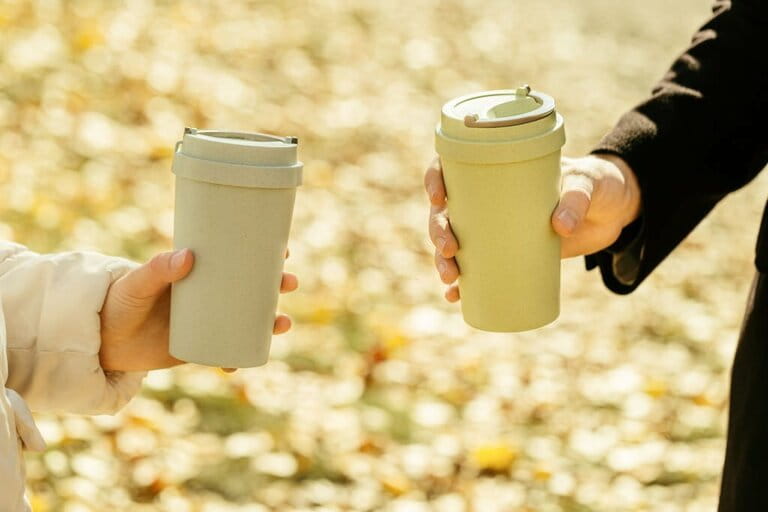 Man holding in hand bamboo cup with lid on autumn blurred background with bokeh, zero waste concept